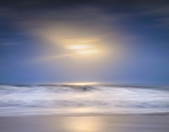 An impressionist blue seascape featuring a centered golden sun, soft motion blur, white surf, and a minimalist navy sky.
