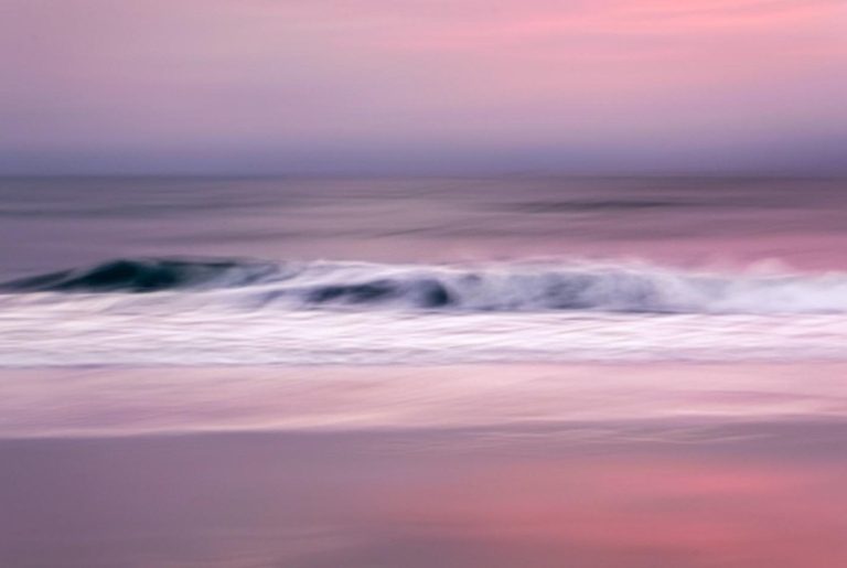 An impressionist long-exposure photograph of a breaking ocean wave at twilight, featuring soft horizontal streaks of lavender and pink.