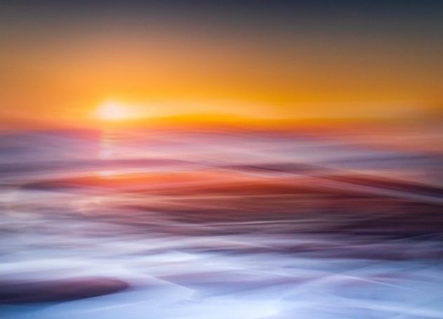 Abstract sunset with horizontal motion blur. A bright sun casting amber and gold flows over fluid, rhythmic streaks of deep blue and violet.